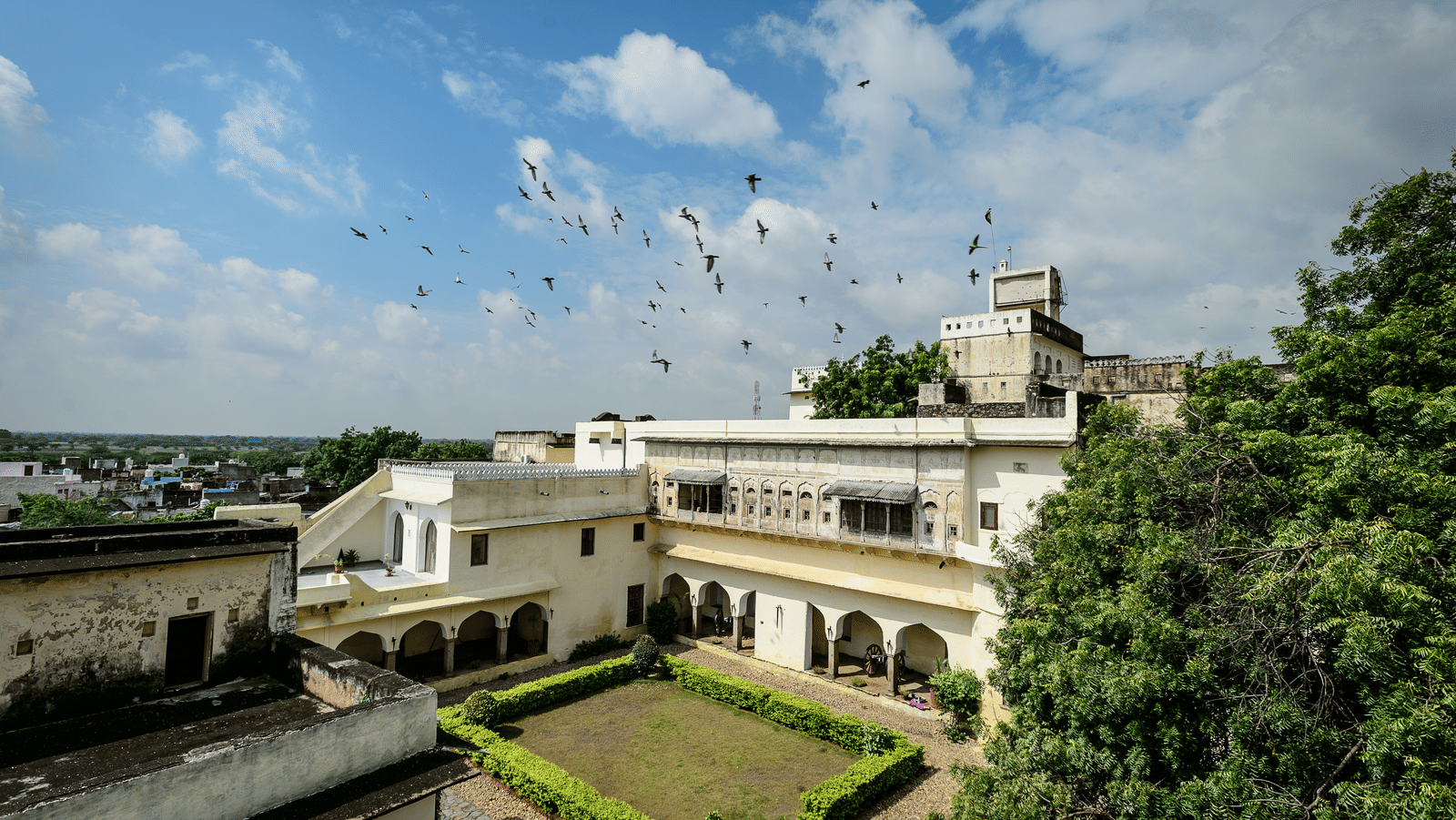 A bird's-eye view of Fort Barli reveals its courtyard, white buildings, and surrounding landscape under a partly cloudy sky.