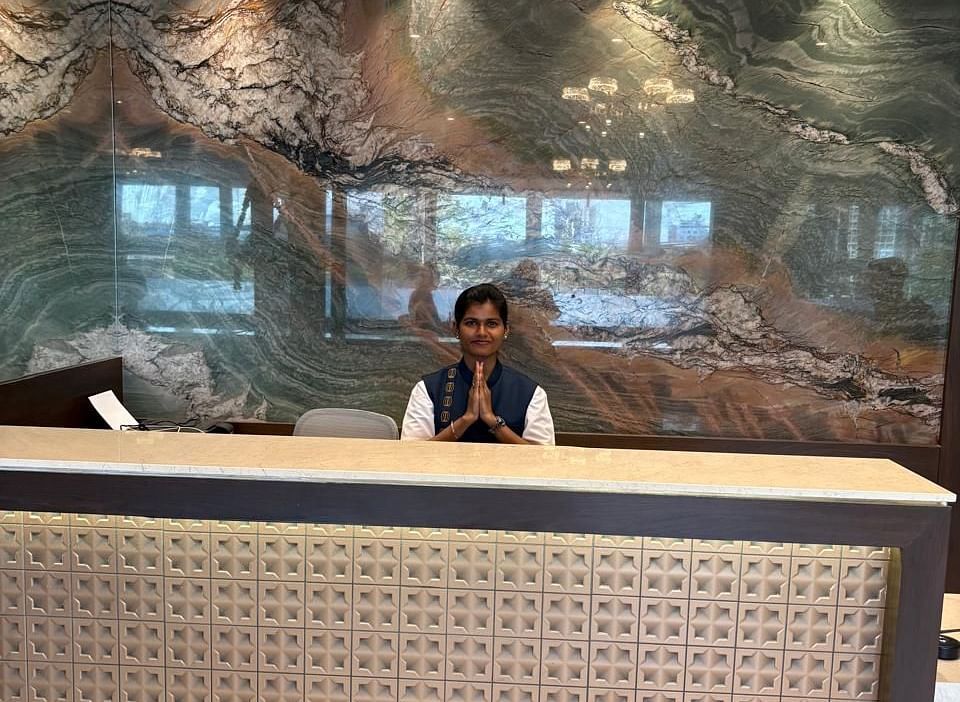 A reception desk with a patterned front and a person standing behind it is visible in a warmly lit interior - Melior Inn
