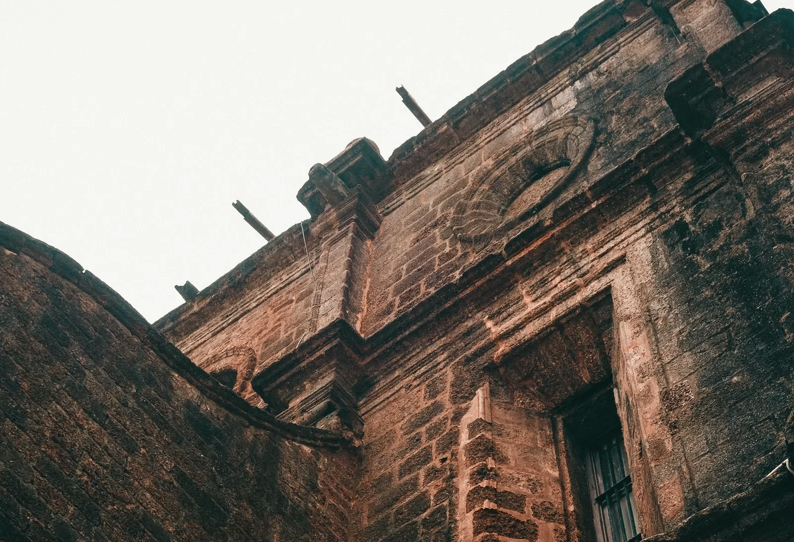 A low-angle view looking up at the weathered stone wall and arched window of an old historic fort or church architecture.