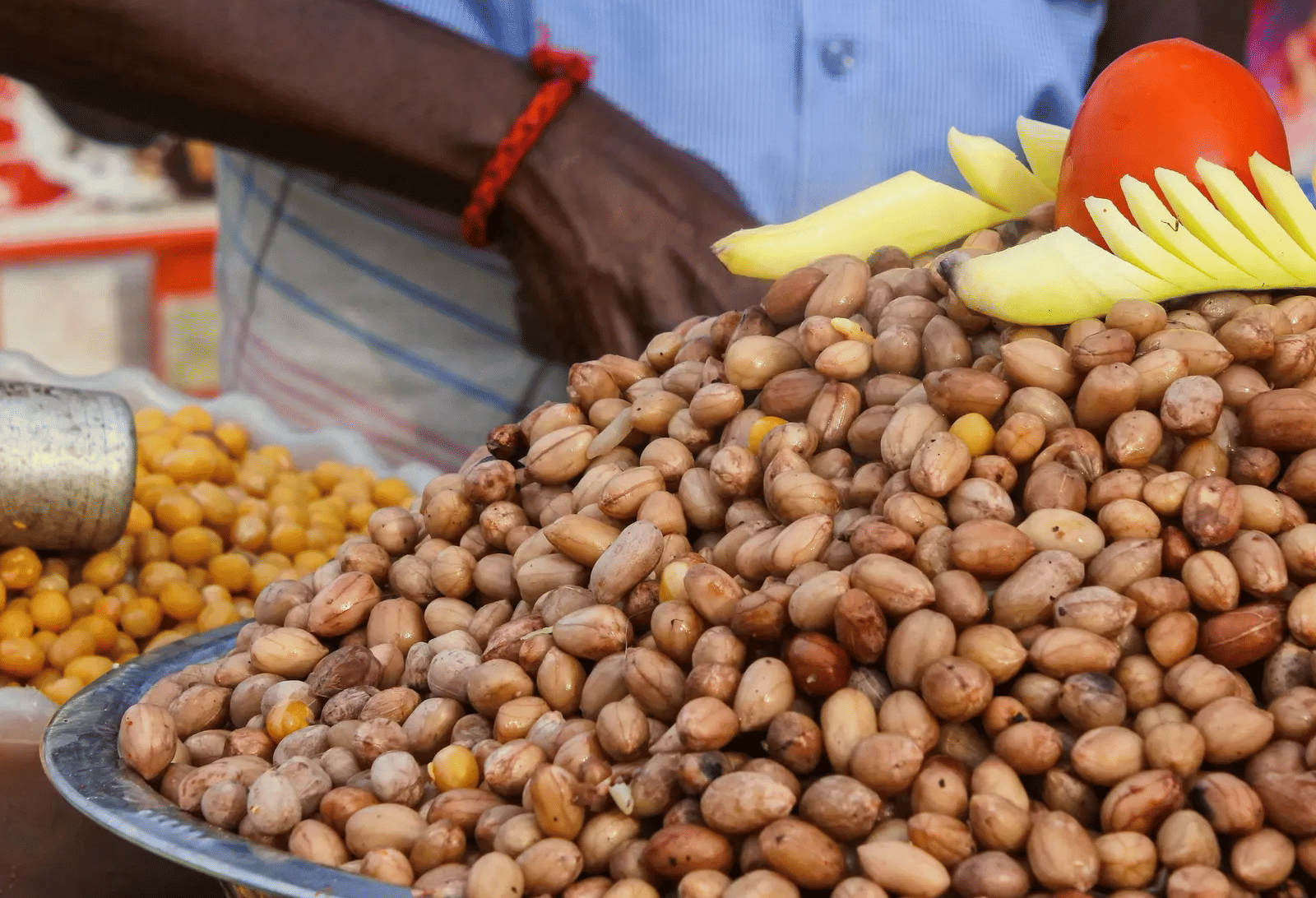 A close-up view of a large metal bowl filled with roasted peanuts sold by a street food vendor.