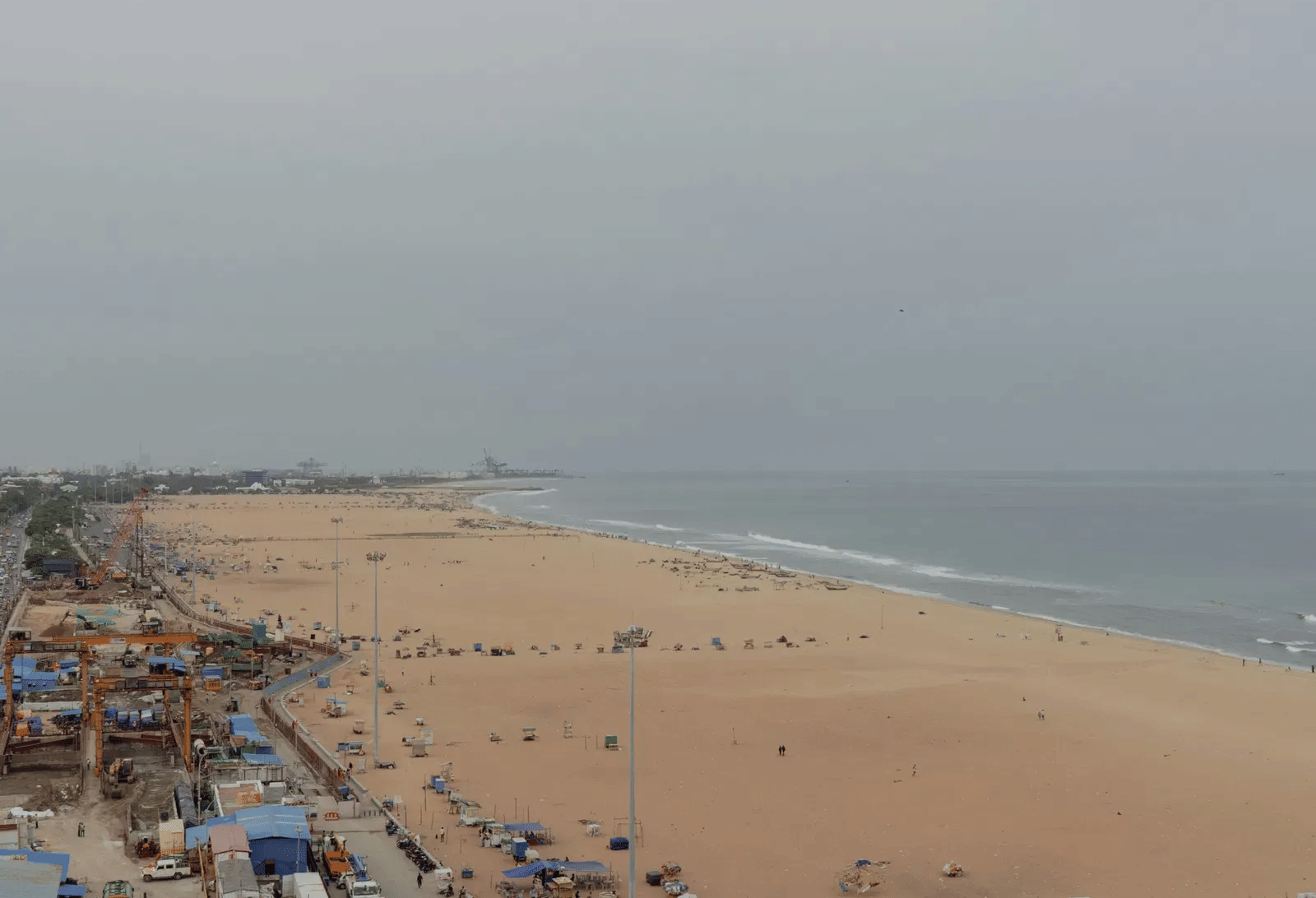 A high-angle view looking down at a vast sandy coastline bustling with colourful market stalls and visitors next to the sea.