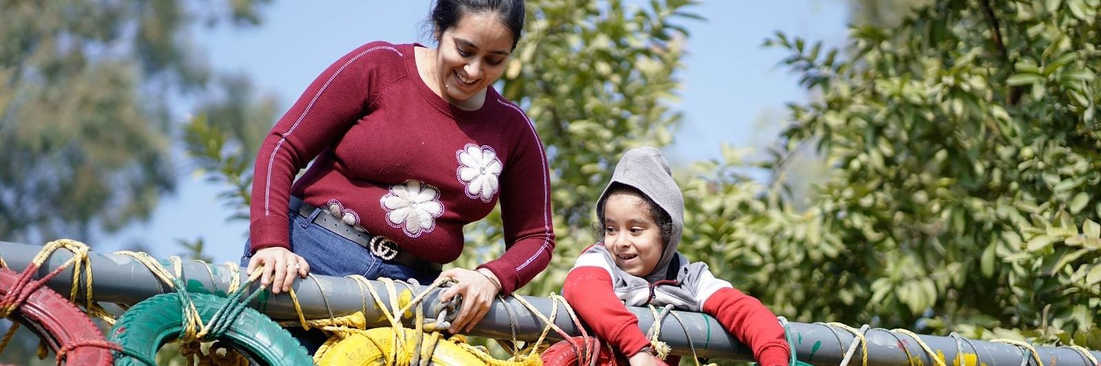 A woman helping a kid with tyre course at inflated trampoline surrounded by trees at Themis Mudhouse - A Nature's Retreat Resort & Wellness