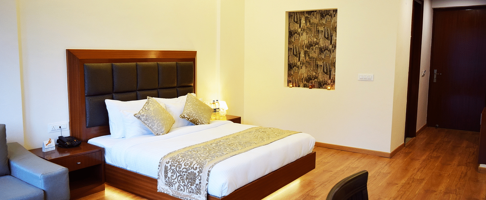 The image shows a hotel room with a large bed, two nightstands, and a couch in the background  | DLS Serenity Resort and Spa
