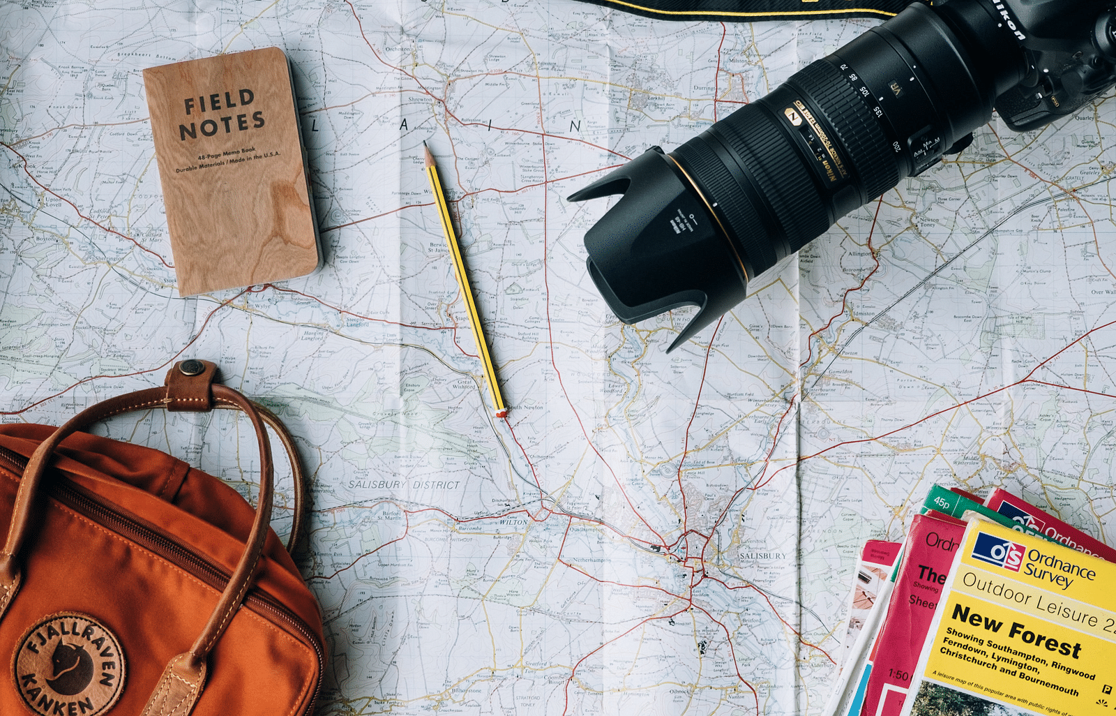 A picture of a camera, a few magazines, a handbag, a diary, and a pencil arranged on a map.