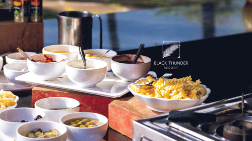 A buffet setup with a variety of dishes laid out for guests, including salads, snacks, and side dishes, against a natural outdoor backdrop - Black Thunder, Coimbatore