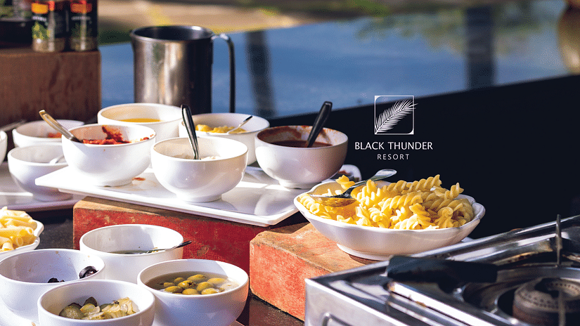 A buffet setup with a variety of dishes laid out for guests, including salads, snacks, and side dishes, against a natural outdoor backdrop - Black Thunder, Coimbatore
