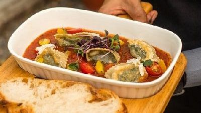 Staff member at Karma Chalets holding a wooden tray with a dish of stir-fried vegetables and two slices of bread.