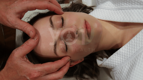 A woman with her eyes closed, receiving a soothing facial massage from the therapist at YO1 Longevity & Health Resorts