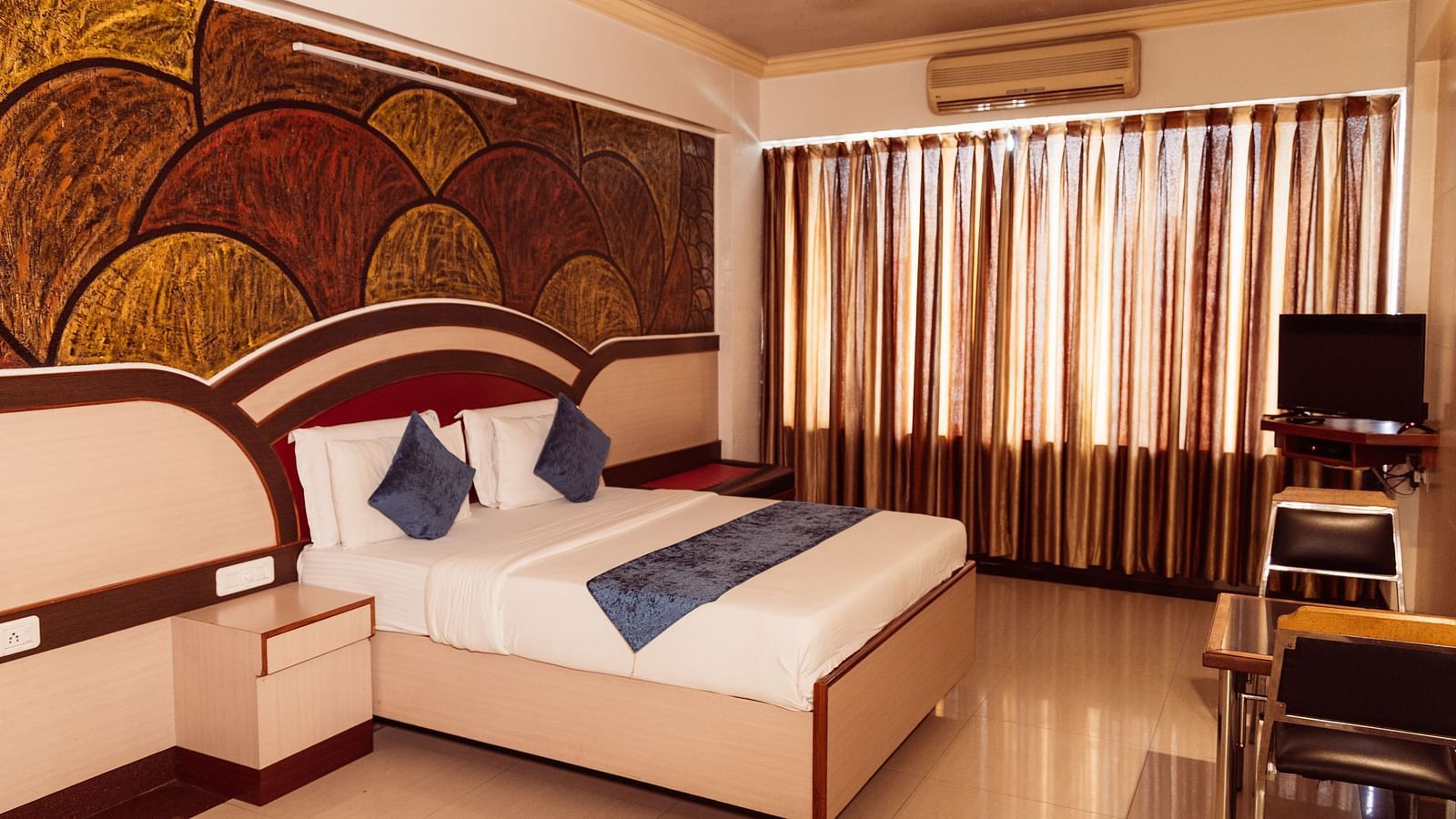 full view image of the executive room at the grand krishna room in bengaluru featuring a double bed and shiny curtains at the far end of the room
