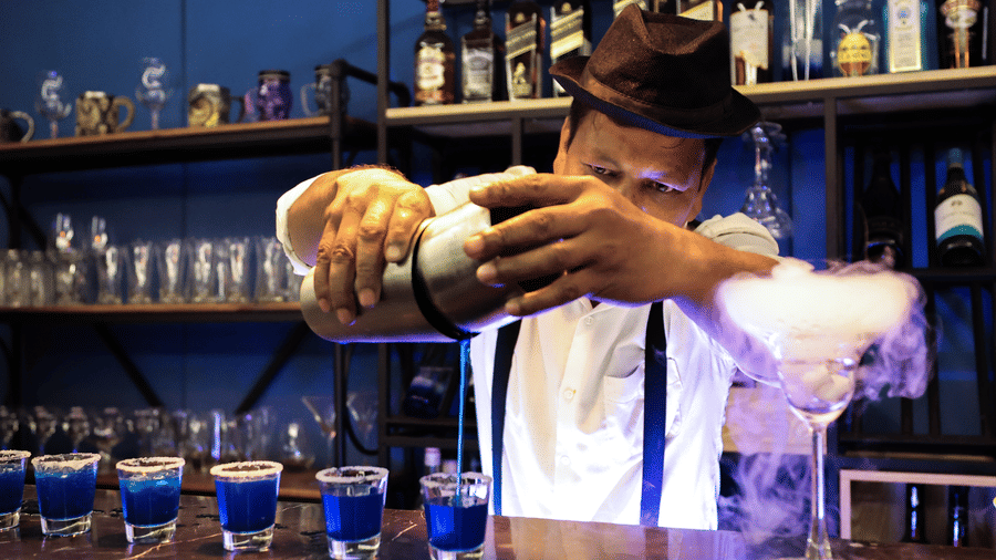 A bartender in a hat and braces adding dry ice to blue cocktails, creating a smoky, theatrical effect at Hotel Hukam's Lalit Mahal.