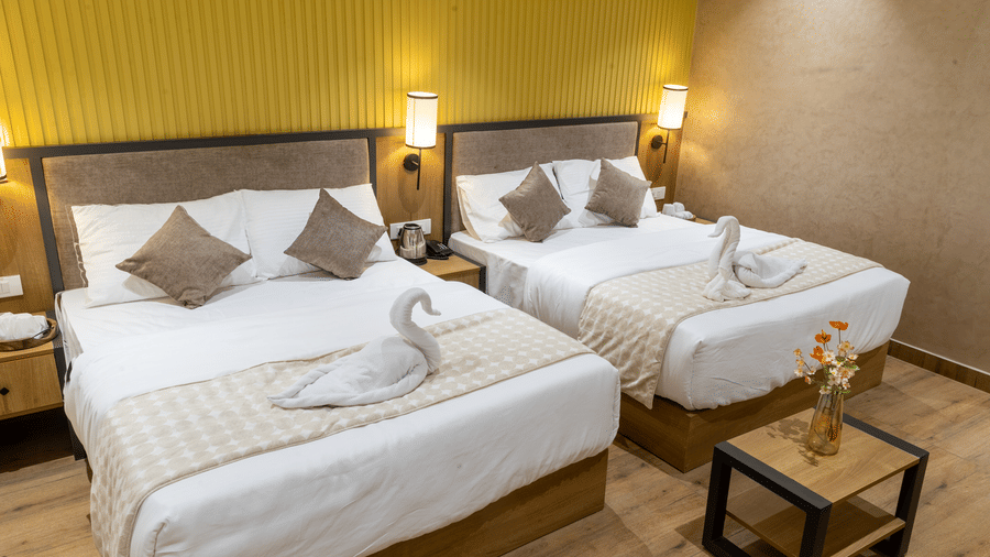 Twin beds neatly arranged with swan towel art in a hotel room featuring warm yellow wall panels.