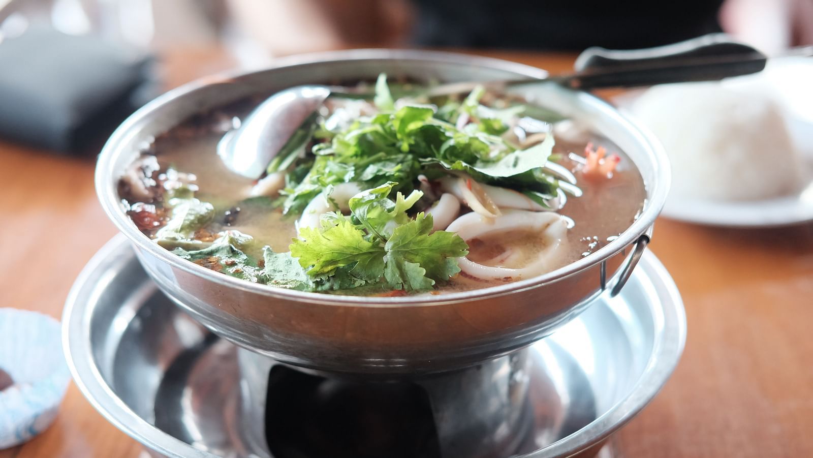 A close up of Tom Yum Goong kept on a bowl on a table with garnishing on top.