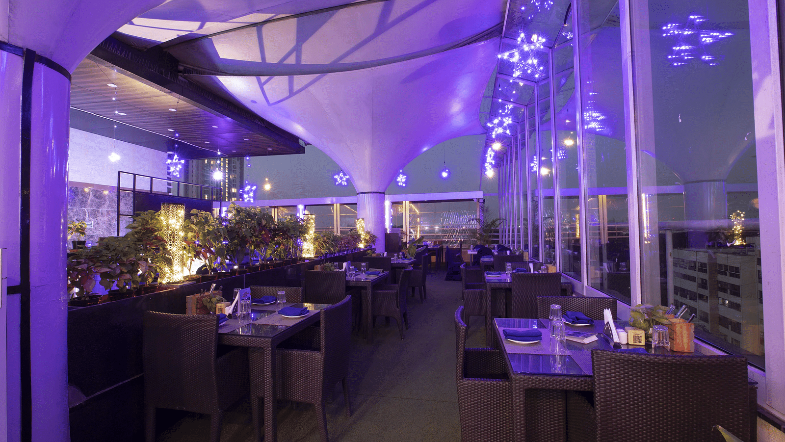 Skylit Rooftop Restaurant with glass walls, ambient purple lighting, neatly arranged tables, and city views, creating a vibrant and upscale dining atmosphere at The Cunningham Hotel