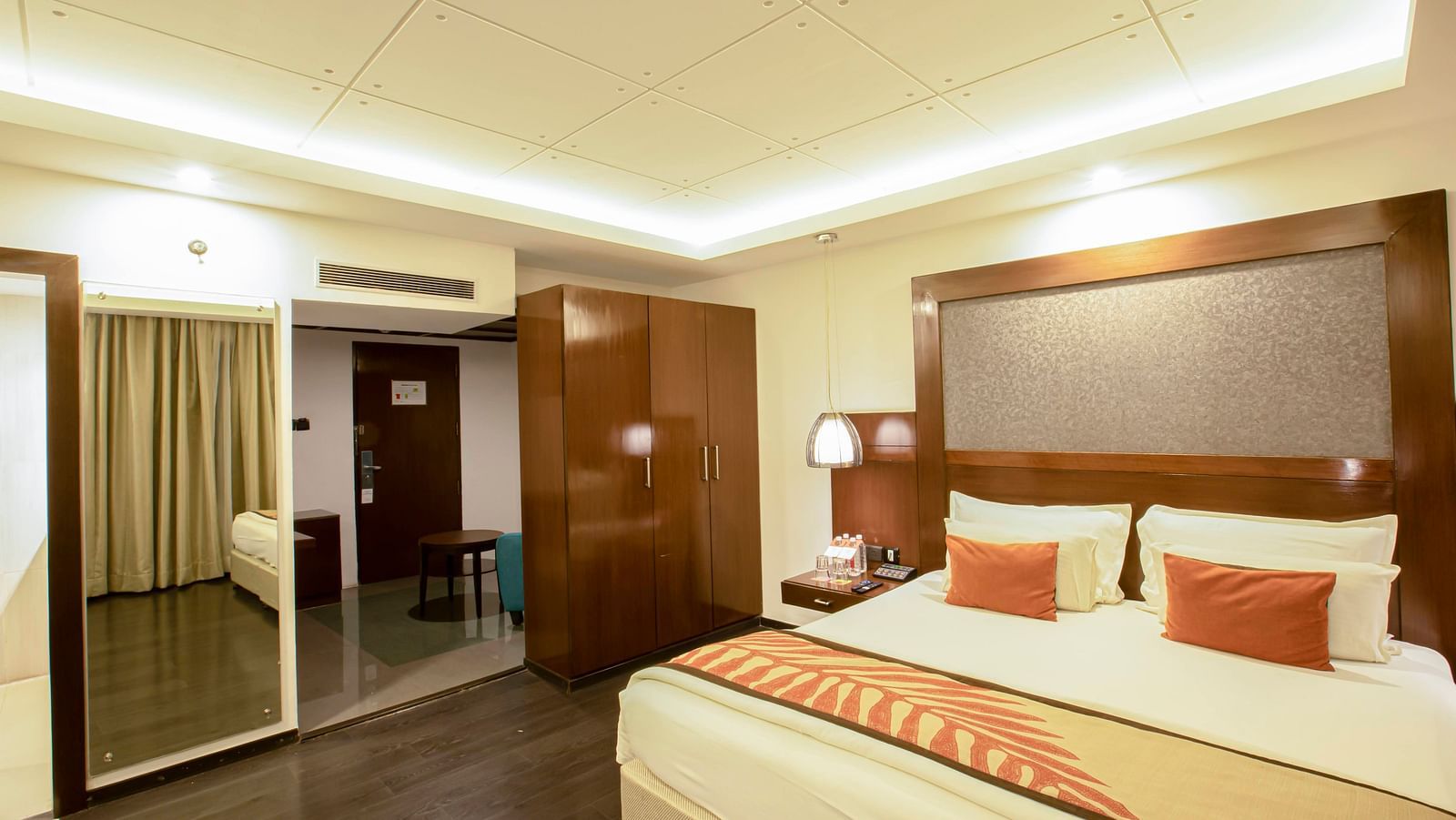 Studio Room at The Cunningham Hotel with warm lighting, a plush bed with a large headboard and a mirror attached to wall next to the wardrobe
