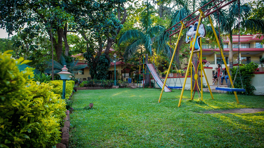 The garden in the property adorned with trees and shrubs featuring a kids' swing and slides.
