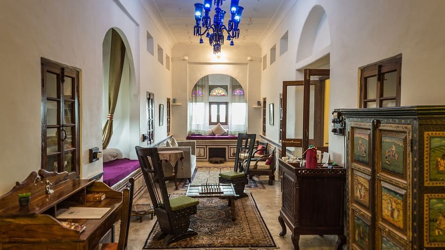 A spacious room at Fort Barli, featuring a blue chandelier, antique furniture, and arched doorways, blends historical charm with modern comfort.