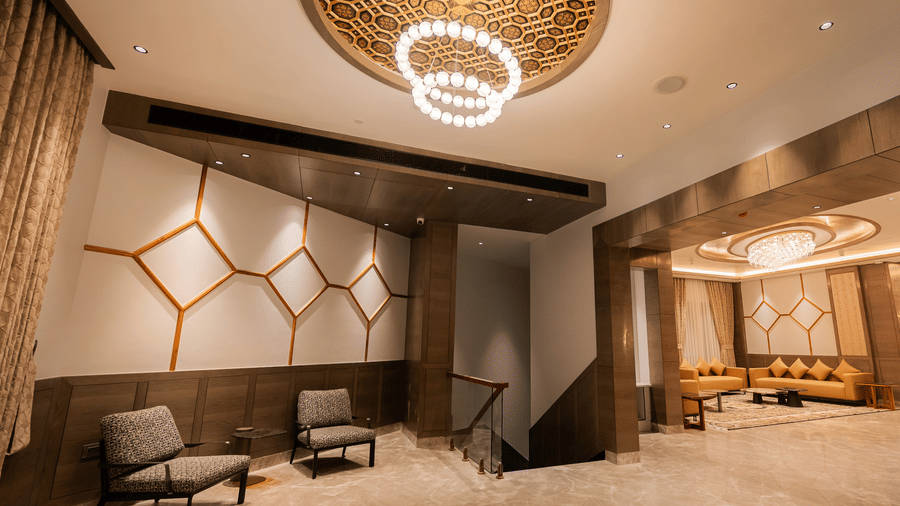 A modern lobby seating area with contemporary chairs and a circular chandelier under a geometric ceiling at Ananta Express, Katra.