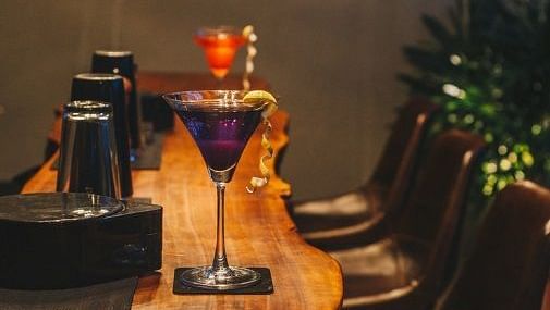 Side view shot of the bar counter featuring a martini glass with purple coloured cocktail.