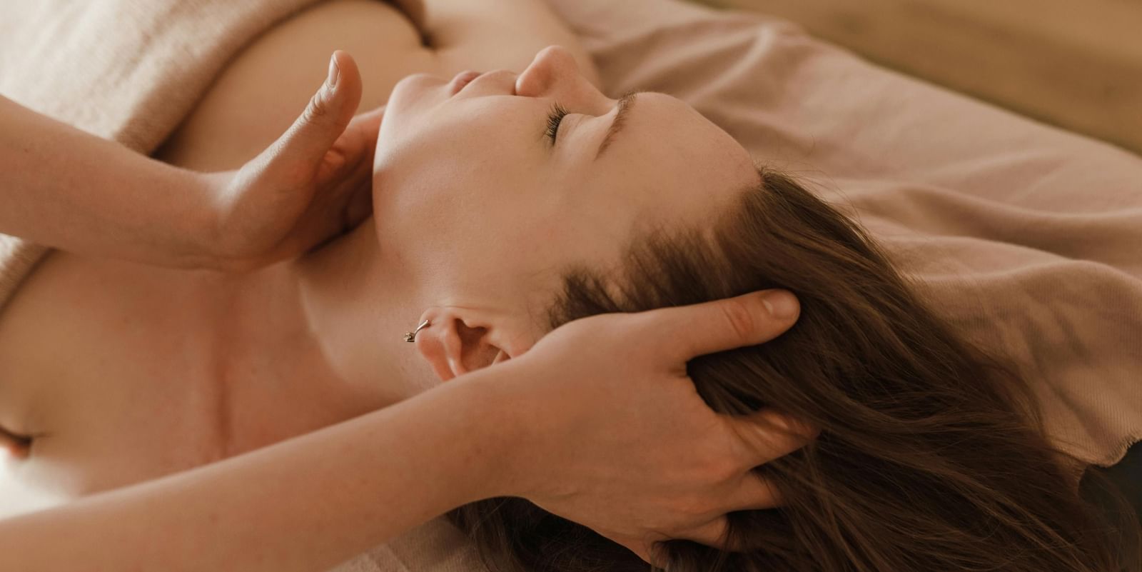  A client with her eyes closed lies on a massage table as a therapist gently massages her neck and head.