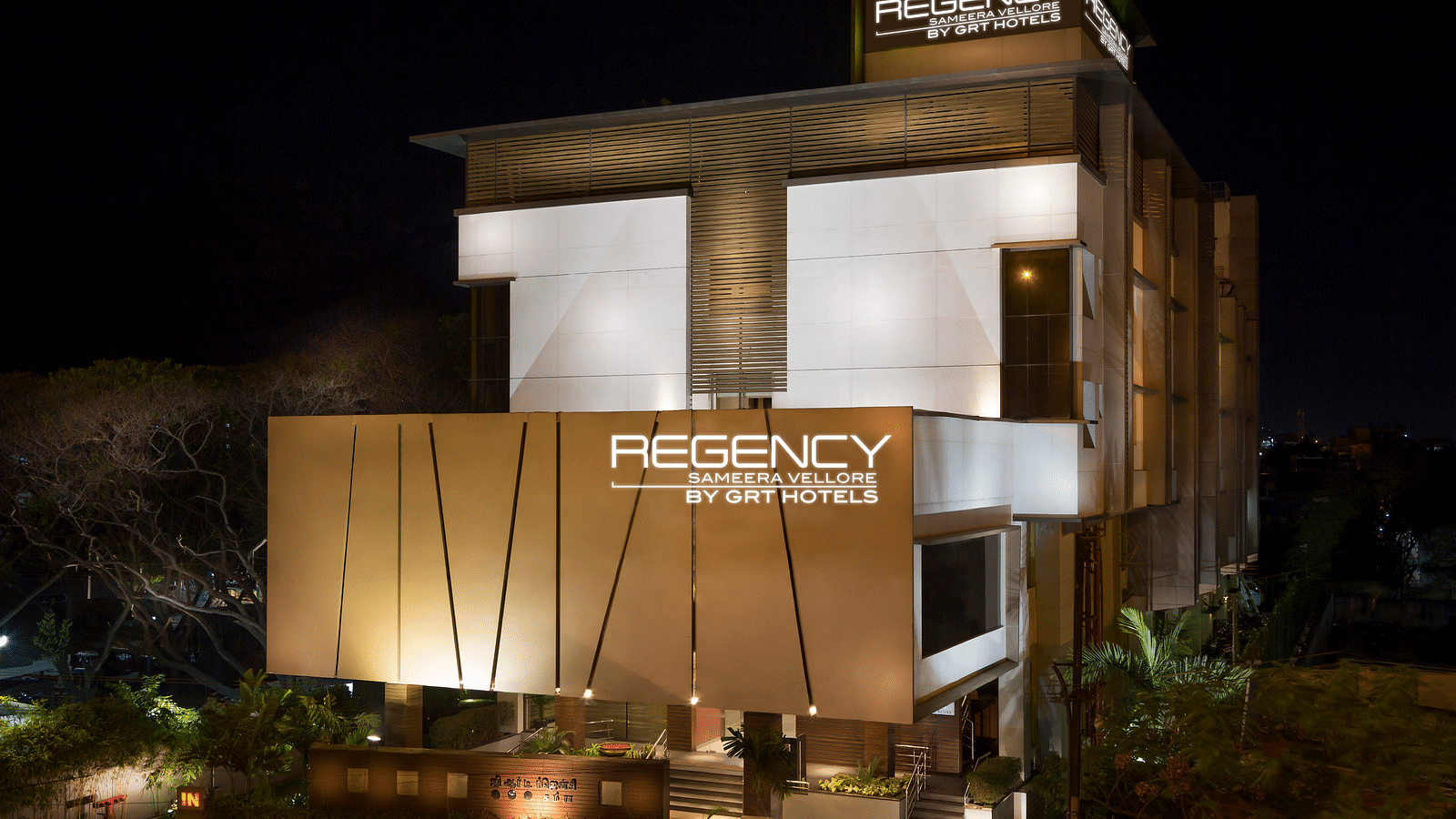 Modern multi-story hotel building with warm lighting, a prominent hotel sign, and landscaped grounds