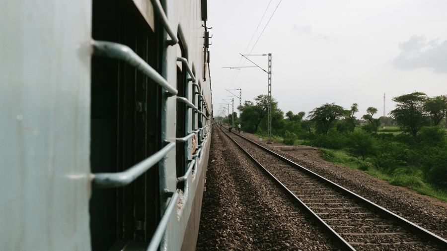 Side shot from a moving train window showing parallel railway tracks running alongside green fields.