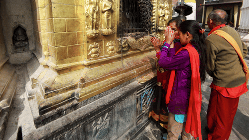 Devotees offering prayers at a beautifully carved, golden temple wall.