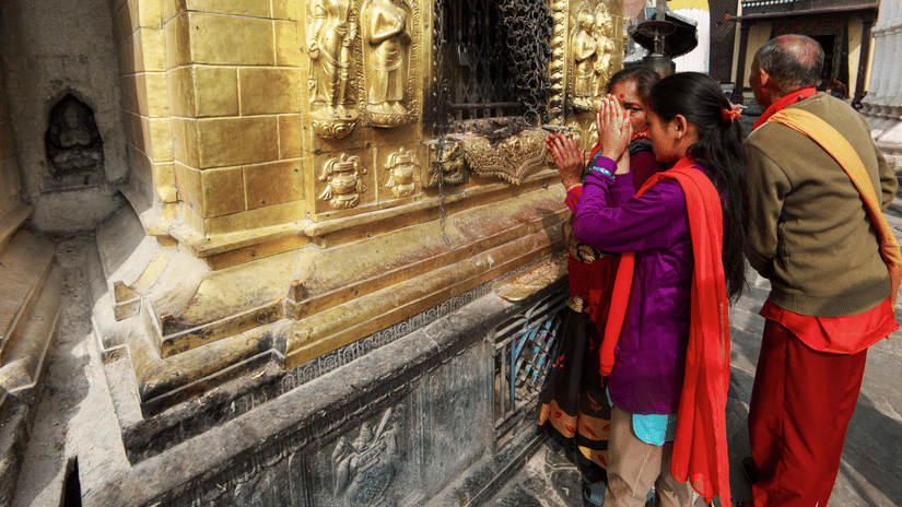 Devotees offering prayers at a beautifully carved, golden temple wall.