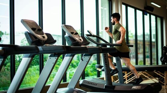 A man running on a treadmill in a gym with several other treadmills in the view.
