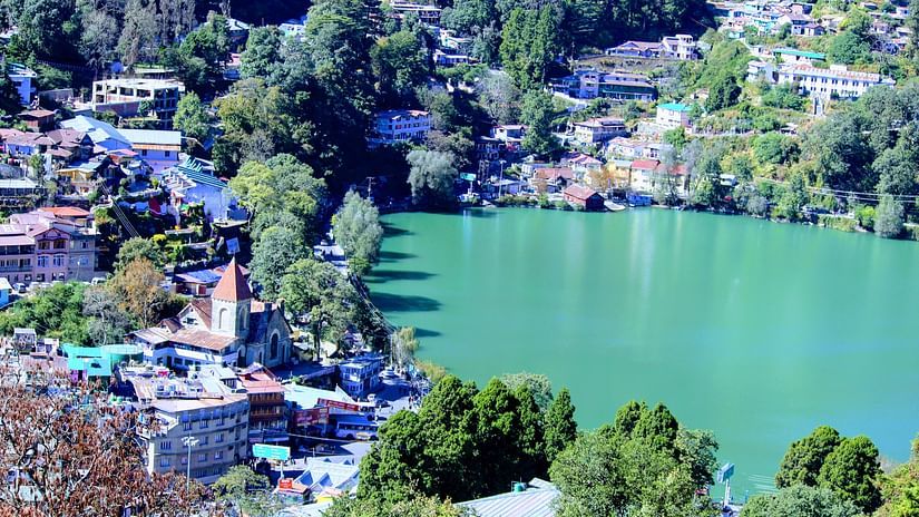 A vibrant green lake nestled amidst a densely populated hillside with colorful houses and lush trees, reflecting the surrounding architecture and natural beauty under a bright sky