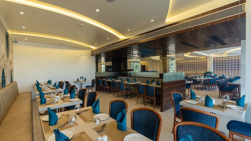 Long view of the elegant restaurant at Mastiff Grand The Sia Palace Suites & Banquets, Khopoli, with many set tables, plush seating, and modern decor.