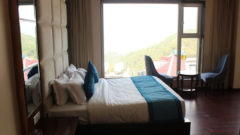 An image of a bedroom featuring a double size bed, a seating area with two sofa chairs and centre table, and an open window next to it - Mastiff Hotel, Dalhousie