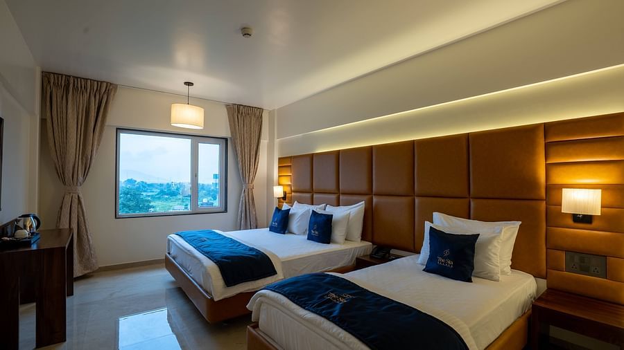 Side view of two beds in Family Premium with bedside tables scenic view from windows with curtains - Mastiff Grand - The Sia Palace Suites Banquets Khopoli