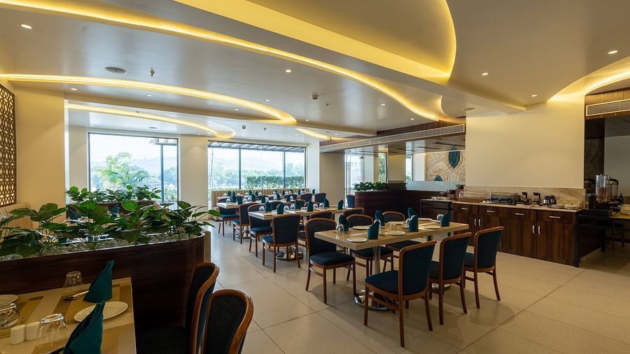 Spacious restaurant interior at Mastiff Grand The Sia Palace Suites & Banquets, Khopoli, featuring multiple dining tables, a buffet counter, and large windows with outdoor views.