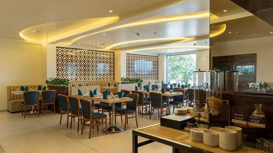 A bright dining room at Mastiff Grand The Sia Palace Suites & Banquets, Khopoli, showing set tables, decorative jali screens, and a buffet station with breakfast items.