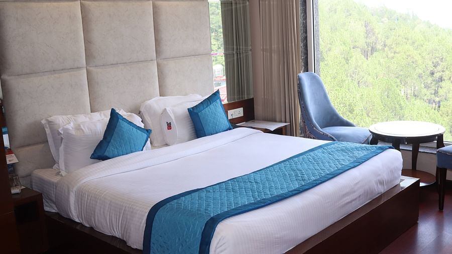 Side view of Deluxe room with plush bed and bedside tables, seating area with coffee table - Mastiff Hotel, Dalhousie