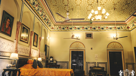 A room at The Umaid Vilas, Jaipur with a double bed, paintings hanging on the wall and a chandelier hanging from the ceiling