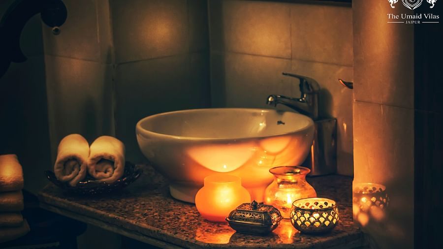 A dimly lit bathroom at Umaid Vilas Jaipur with a white sink, rolled towels, and several lit candles creating a warm, inviting atmosphere.
