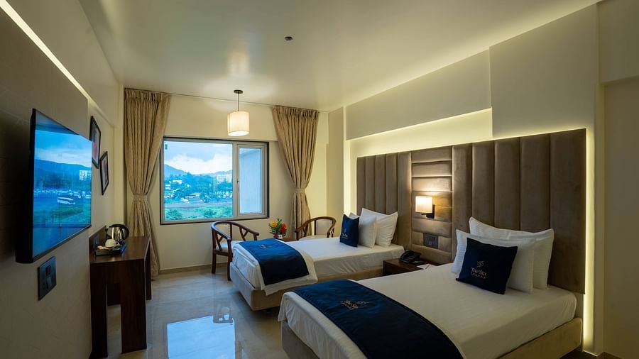 Side view of the Deluxe Twin with twin beds TV set seating area with windows and curtains - Mastiff Grand - The Sia Palace Suites Banquets Khopoli
