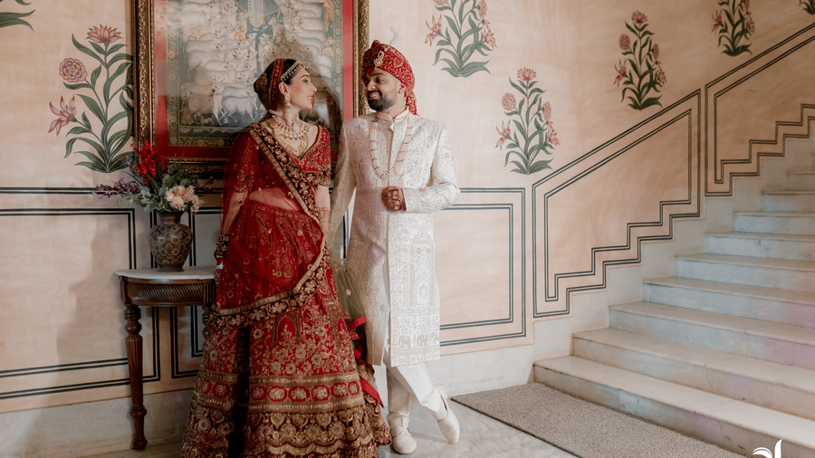 Bride and groom posing by a heritage staircase with floral wall art at Umaid Palace.