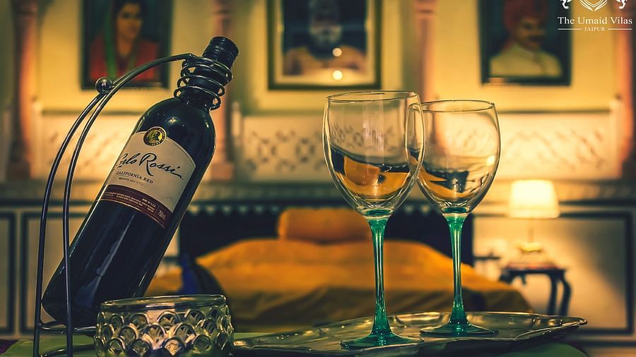 A bottle of wine and two glasses set on a tray in a room at Umaid Vilas Jaipur, with artwork visible in the background.