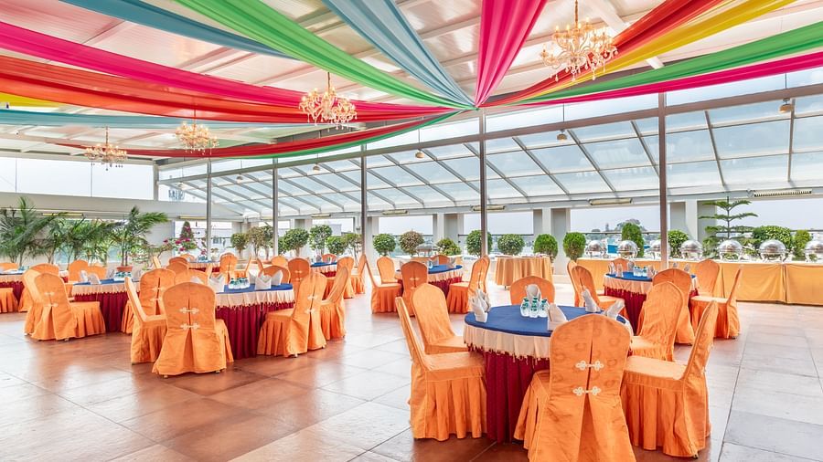 A spacious room with round tables and chairs, decorated with colorful fabric draping from the ceiling. Large windows provide natural light- TGI Grand Fortuna, Krishnagiri Main Road, Hosur