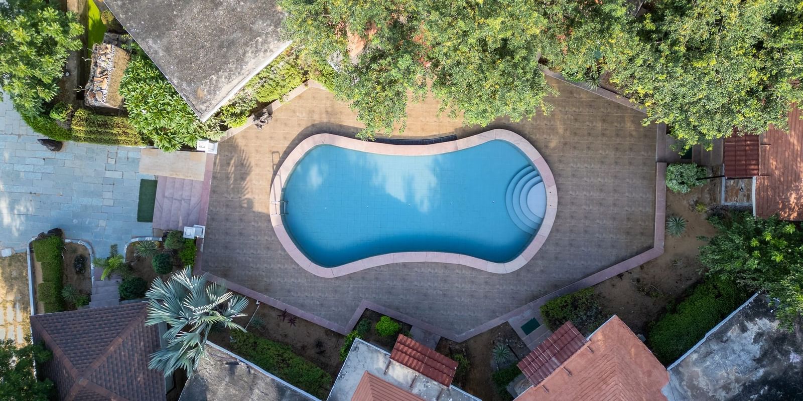 Aerial view of a swimming pool at Valley by Grassfield, nestled among lush trees and surrounded by accommodations.