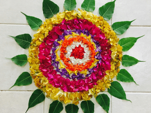 Vibrant floral pookalam with layered flower petals and green leaves arranged in symmetrical patterns for Kerala’s Onam festival celebrations