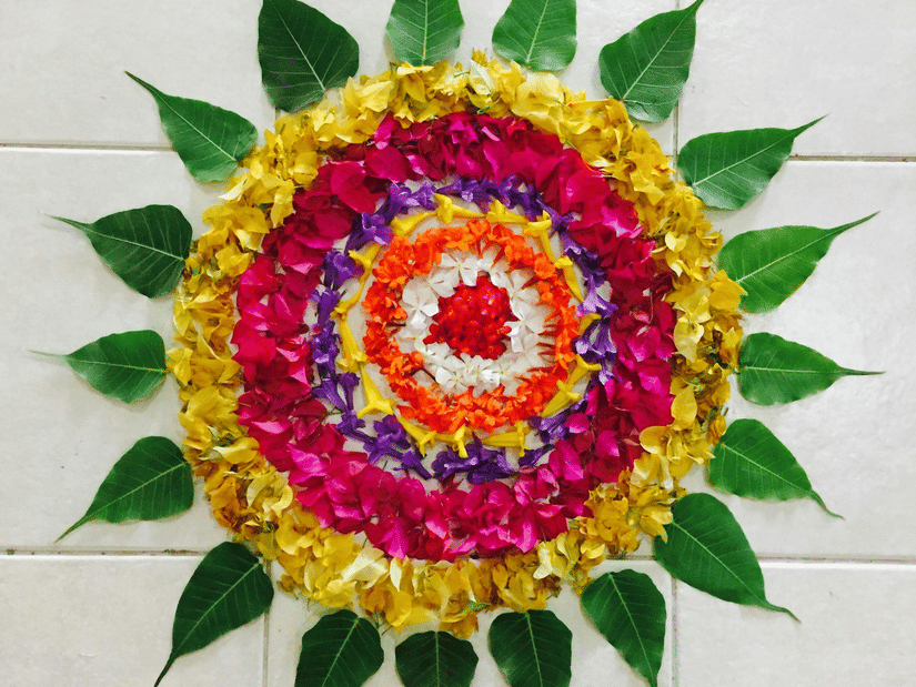 Vibrant floral pookalam with layered flower petals and green leaves arranged in symmetrical patterns for Kerala’s Onam festival celebrations