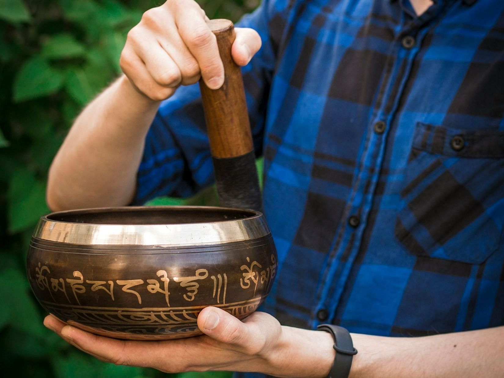 An image of a person holding a gong and a metal vessel to creating a vibrating sound and soothing aura