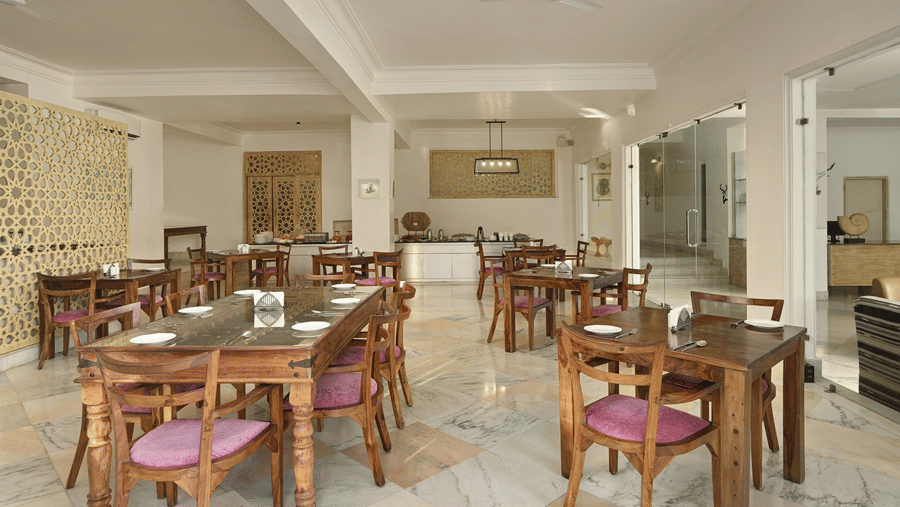 A restaurant at Fateh Safari Resort, Kumbhalgarh featuring tables and chairs and a kitchen counter with plates, cutlery, bowls, jugs, etc.