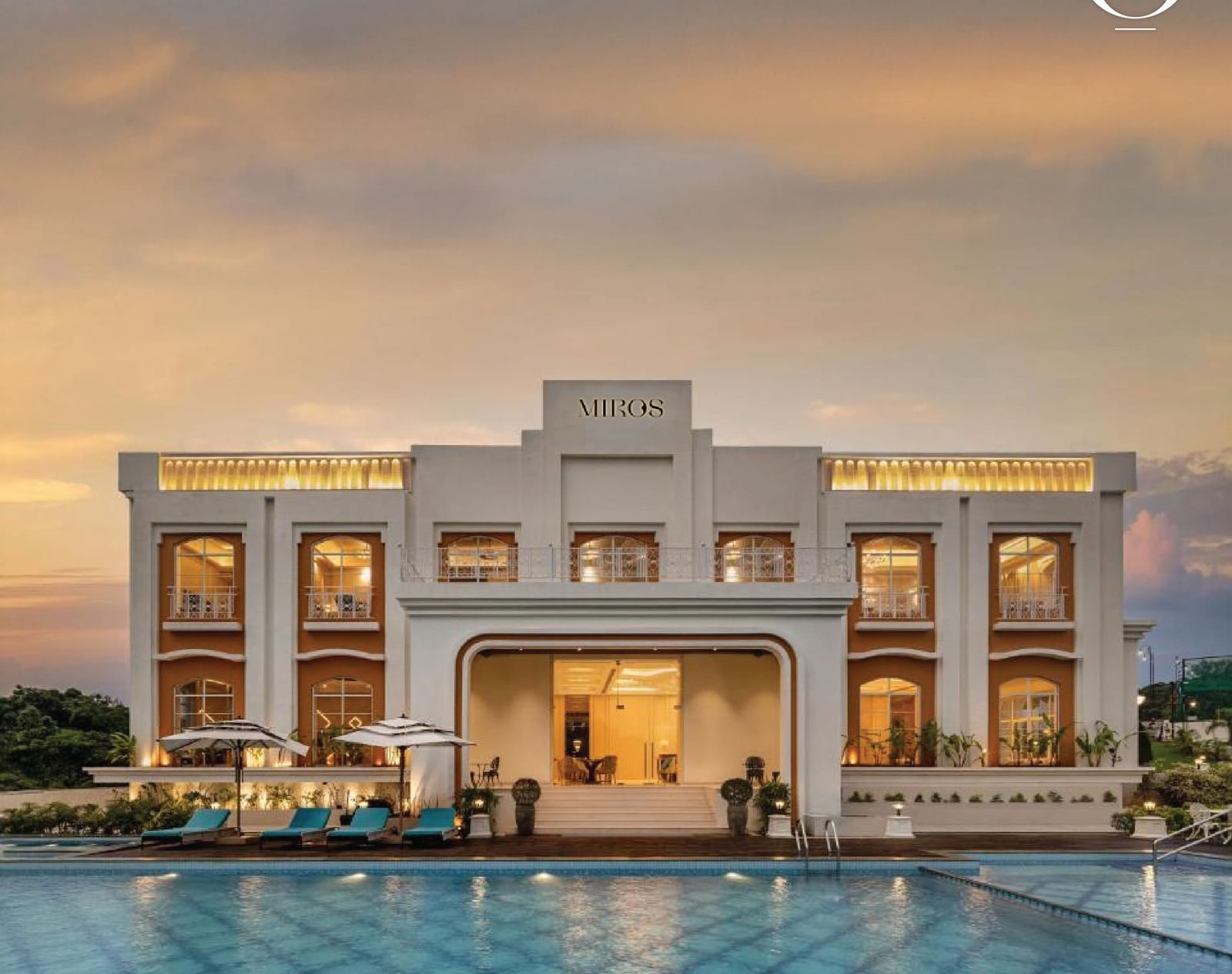 A full view facade of the best resort in Goa, MIROS Hotels with a calm swimming pool in the foreground along with beautiful sunset sky in the background.