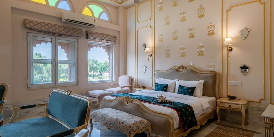 Maharaja Suite at Umaid Palace featuring a lavish bedroom with king size bedside table and lamps on either side. The room also have few soft sofa chairs an, a table, and a window near AC.