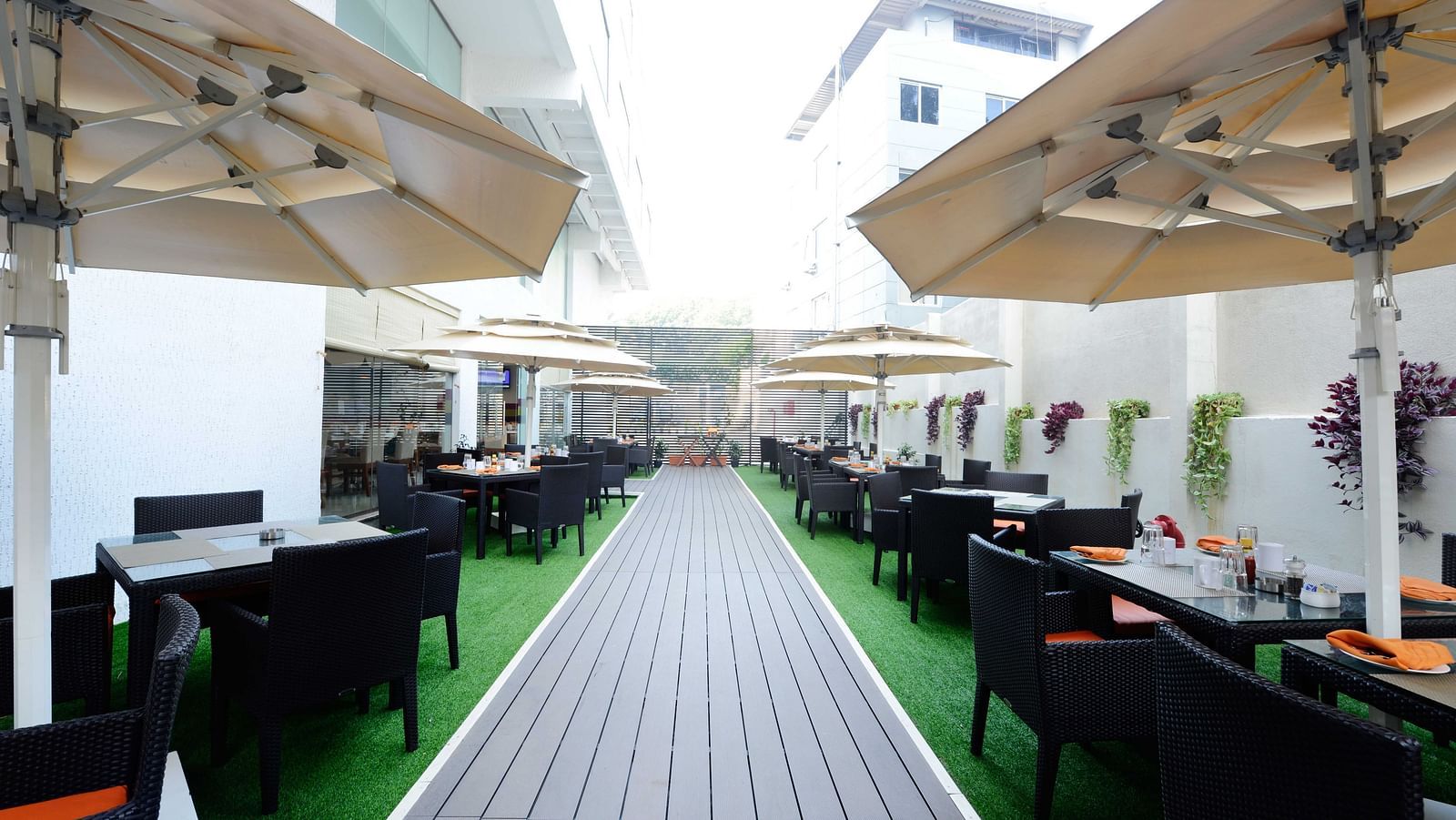 Coffee Shop at The Cunningham Hotel featuring outdoor dining space with black wicker furniture, green flooring, large umbrellas, and elegant table settings featuring orange napkins