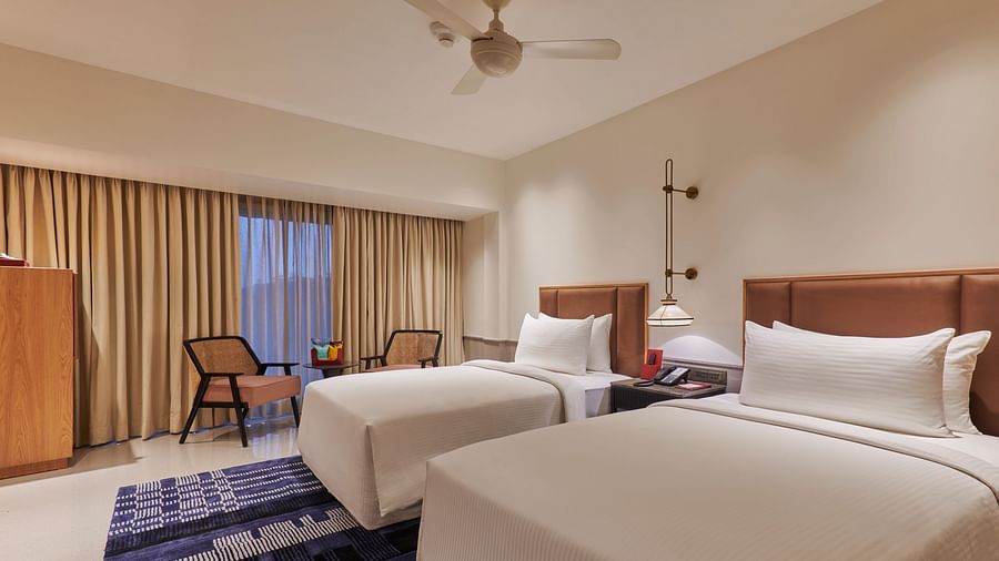 A hotel room with two twin beds, a colorful rug, a dresser, and a view through a window with curtains - The Dukes Retreat